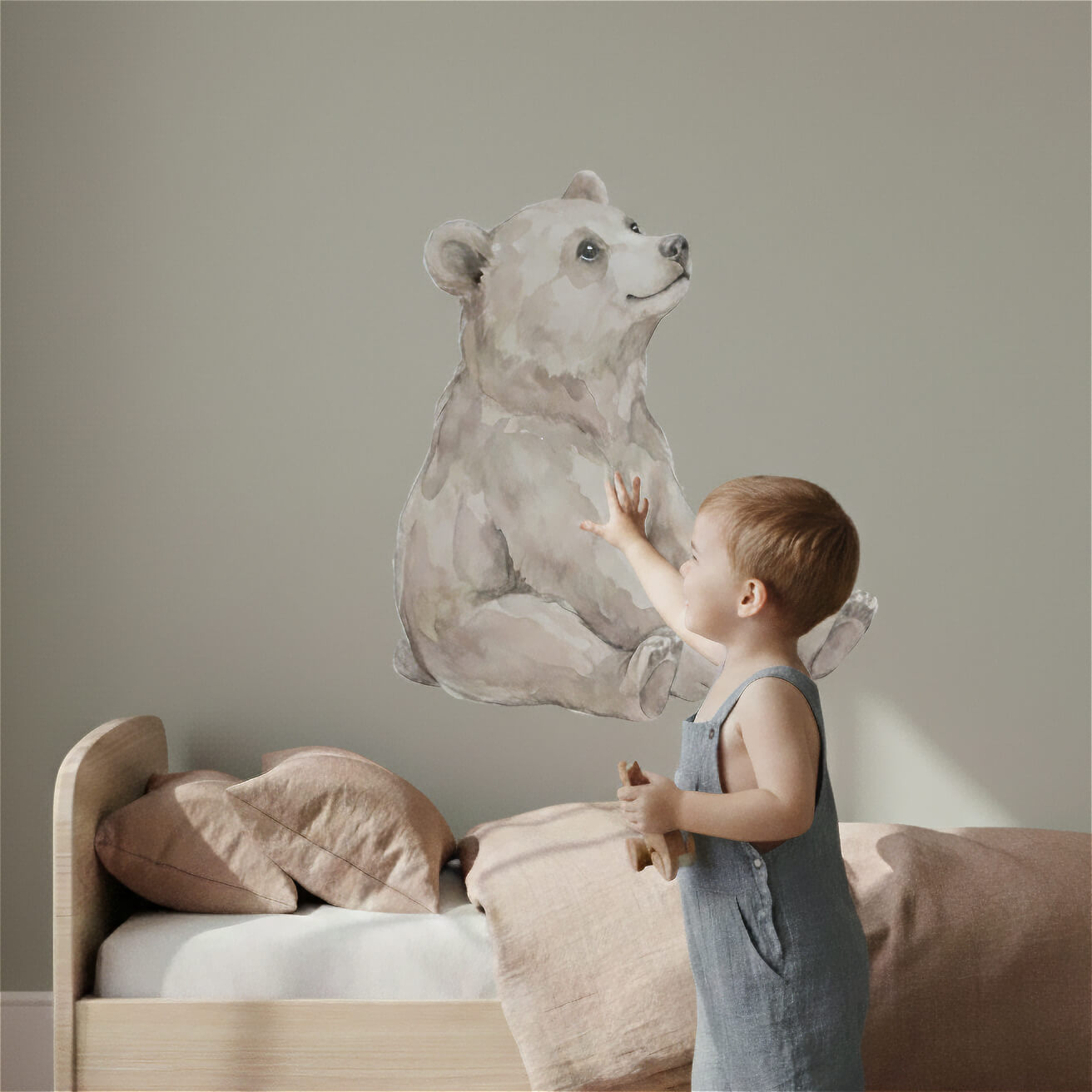 A toddler interacts with our beige watercolor bear wall sticker in a minimalist Scandinavian nursery. The soft illustration and child-friendly scale create a comforting, imaginative environment perfect for baby and toddler rooms.