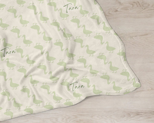 Blanket with green duck pattern and 'Tara' text on a wooden surface