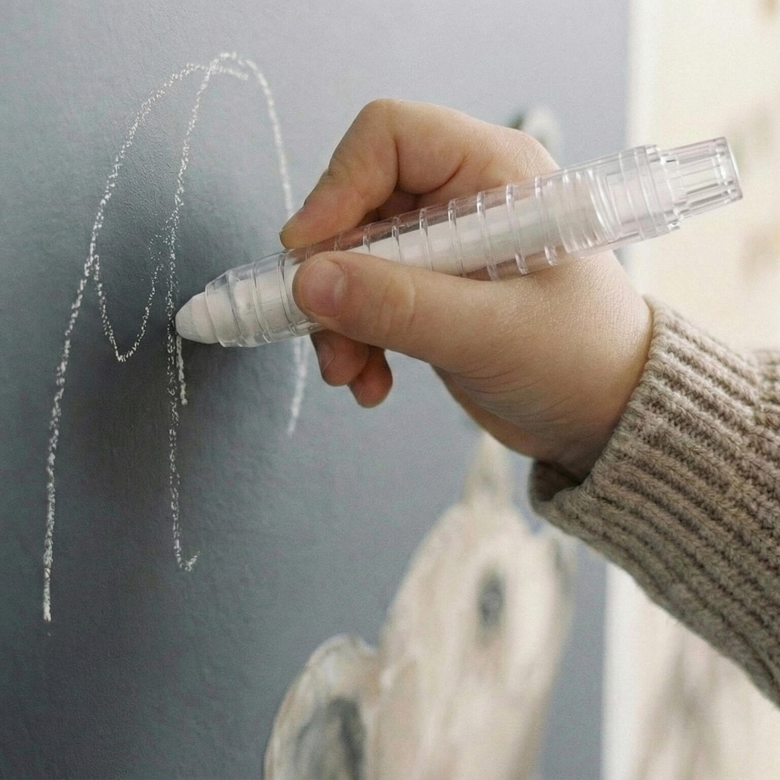 Child drawing with chalk on matte arch wall panel in Montessori play corner