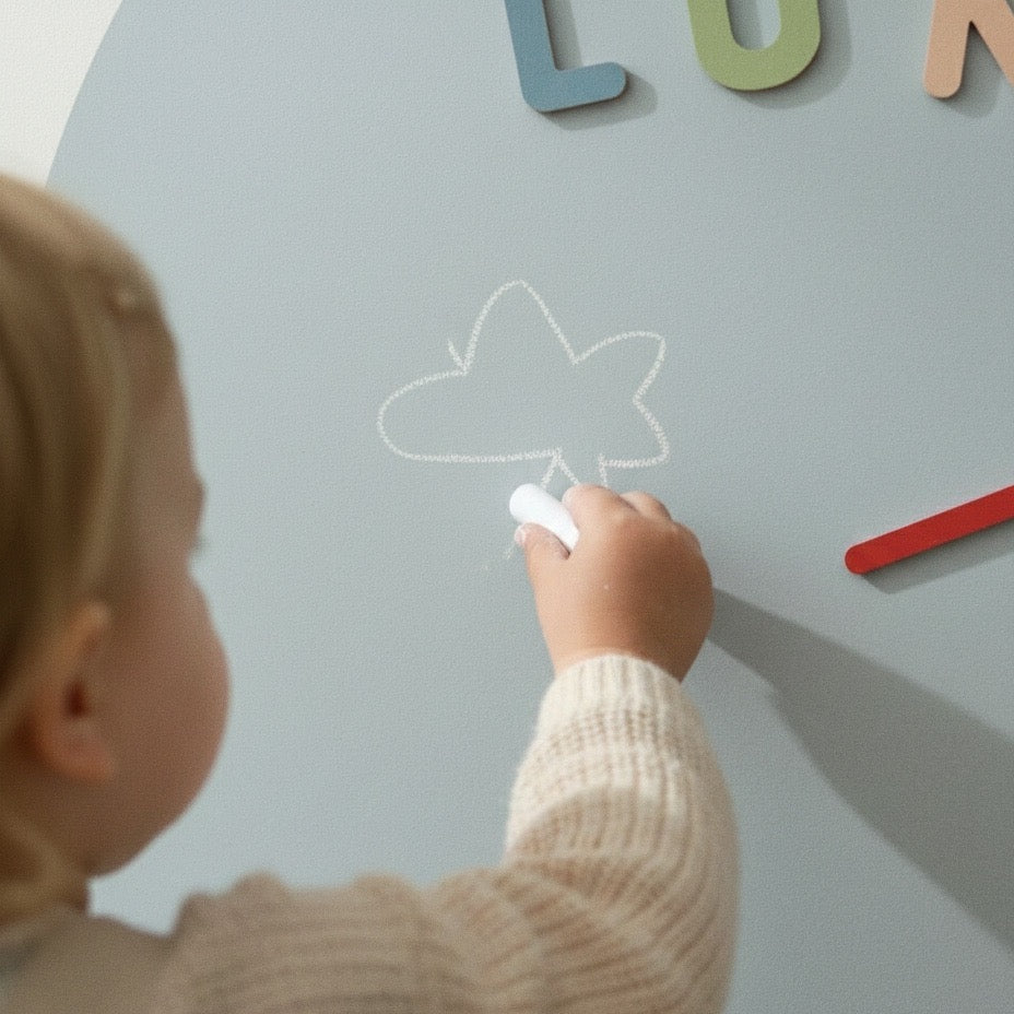Close-up of a child drawing a cloud with white chalk on a blue magnetic arch wall.