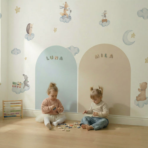 Two toddlers sitting and playing in front of personalized magnetic arch walls with chalk drawings, magnets, and soft nursery wall stickers.