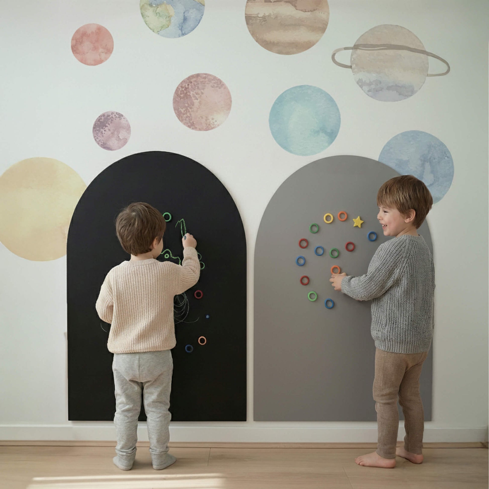 Two toddlers playing with a magnetic arch wall in a calm playroom, surrounded by watercolor space planet wall stickers and colorful magnetic shapes.