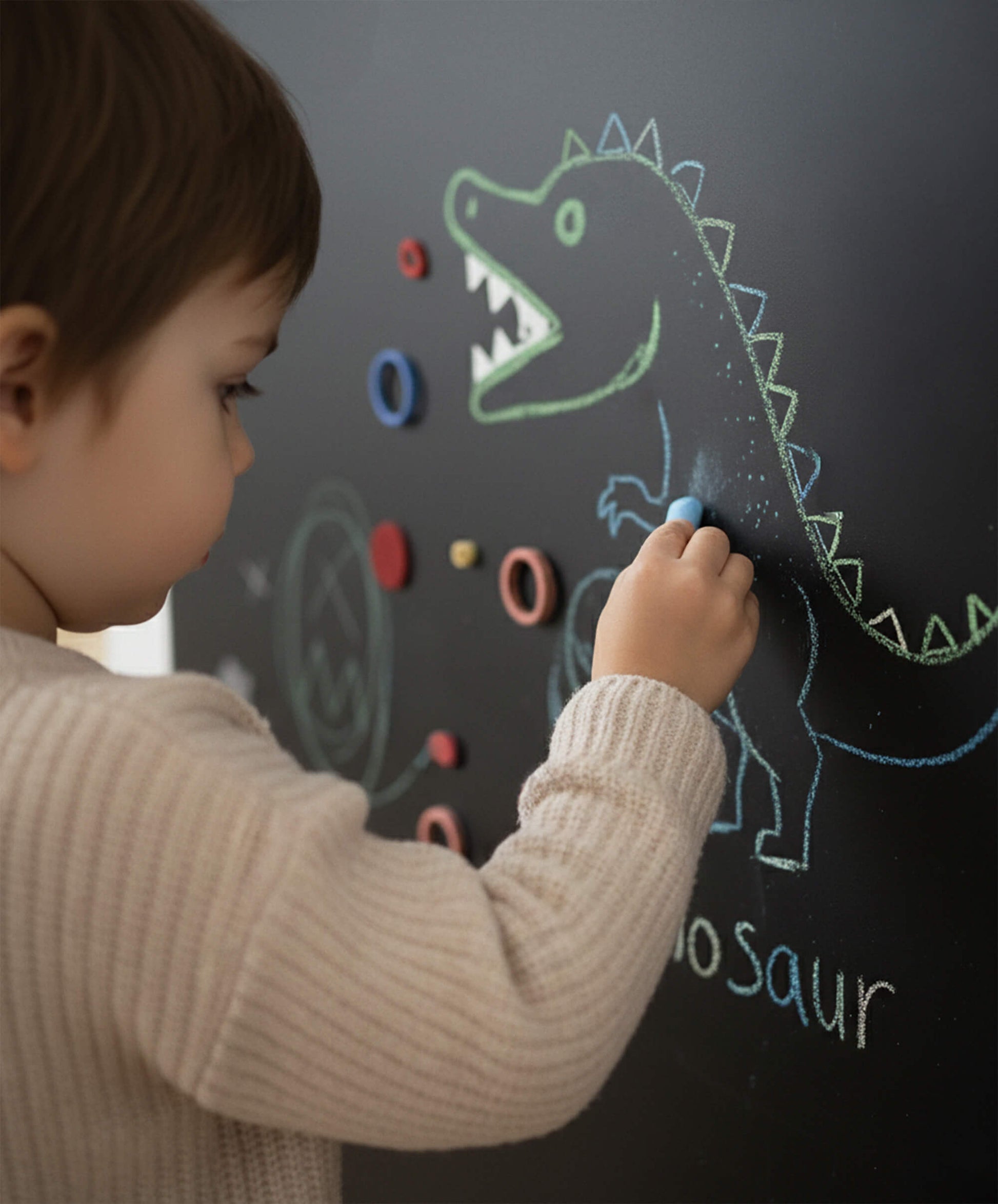 Toddler drawing with chalk on a black magnetic arch wall, using magnets and chalk in a Montessori-inspired play space.