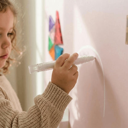 Child holding a white marker writing on a light-colored wall magnetic wall