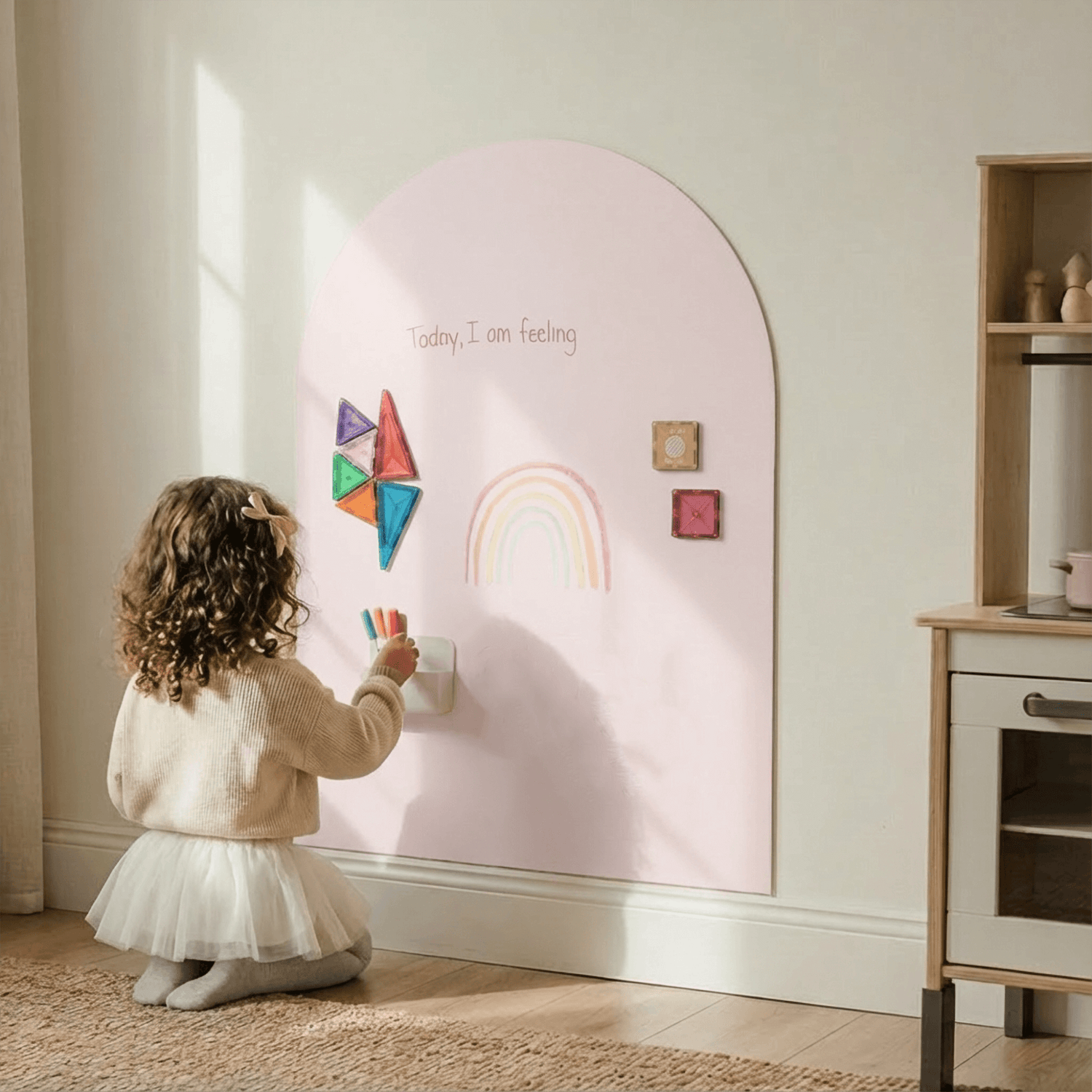 Young child standing in front of pink magnetic arch wall holding colorful markers.