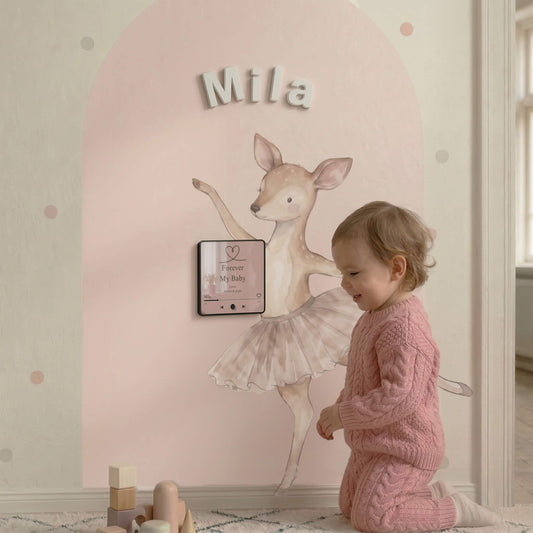 Toddler girl interacting with a pink arched magnetic wall featuring a ballerina decal and personalized sound magnet.
