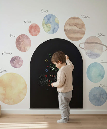 Toddler standing inside a magnetic arch wall with labeled space planet wall stickers in a minimalist children’s playroom.