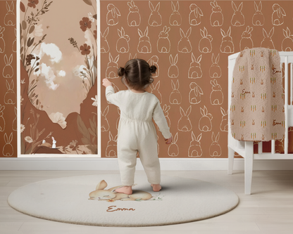 Child in a white outfit standing on a round rug with 'Emma' embroidered, in a room with floral and animal-patterned walls.
