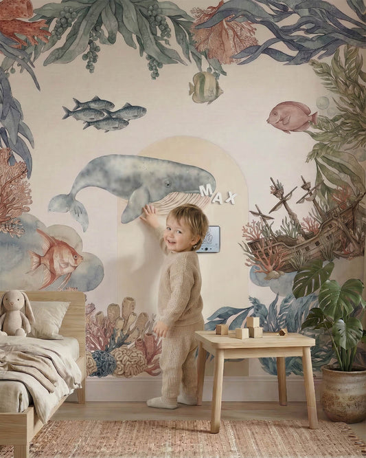 Toddler playing with magnetic alphabet letters on a large watercolor whale wall decal.