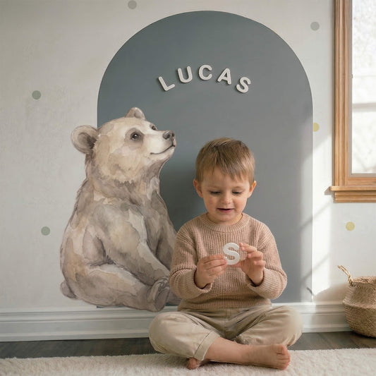 Toddler playing with premium white magnetic letters on a grey arch-shaped magnetic wall canvas in a sunlit nursery.