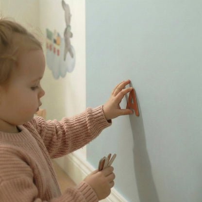 Close-up of a toddler drawing with chalk on a blue magnetic arch wall, showing real chalk texture and hand movement.