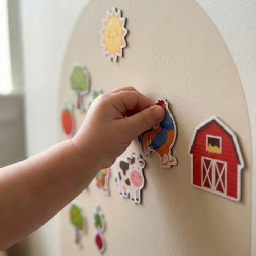 A child's hand placing a rooster magnet onto a beige magnetic arch wall play panel.
