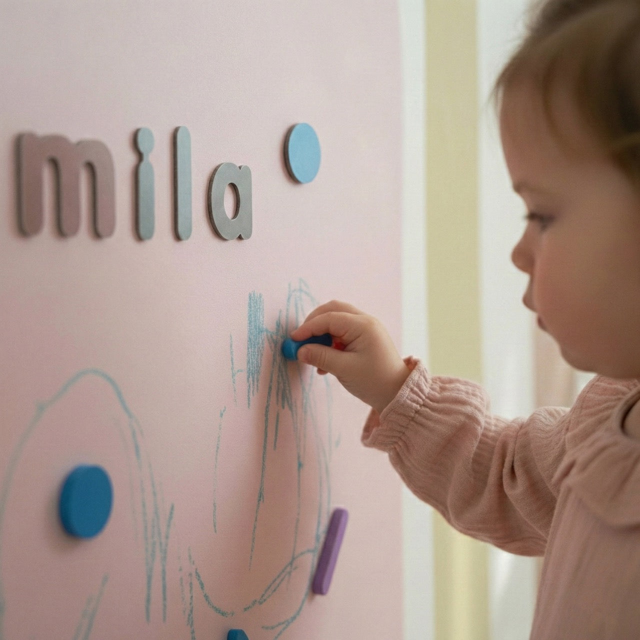 Toddler drawing and placing magnetic shapes on a pastel magnetic wall in a Montessori playroom