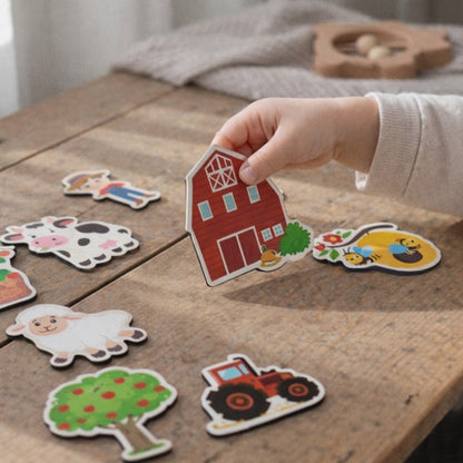 Child's hand holding a farm-themed magnets on a wooden surface with other magnets.