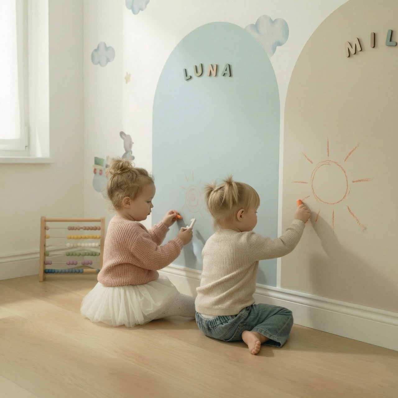 Two toddlers drawing with chalk on pastel magnetic arch walls during creative play in a calm playroom.