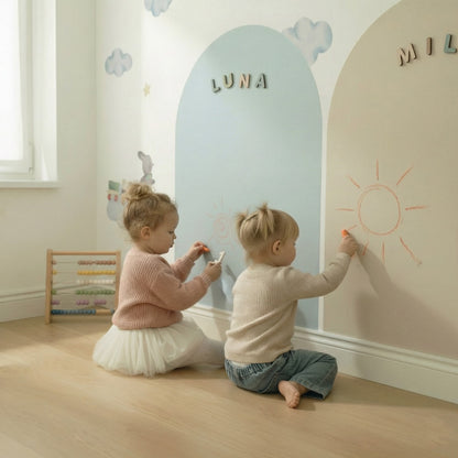 Two toddlers drawing with chalk on pastel magnetic arch walls during creative play in a calm playroom.